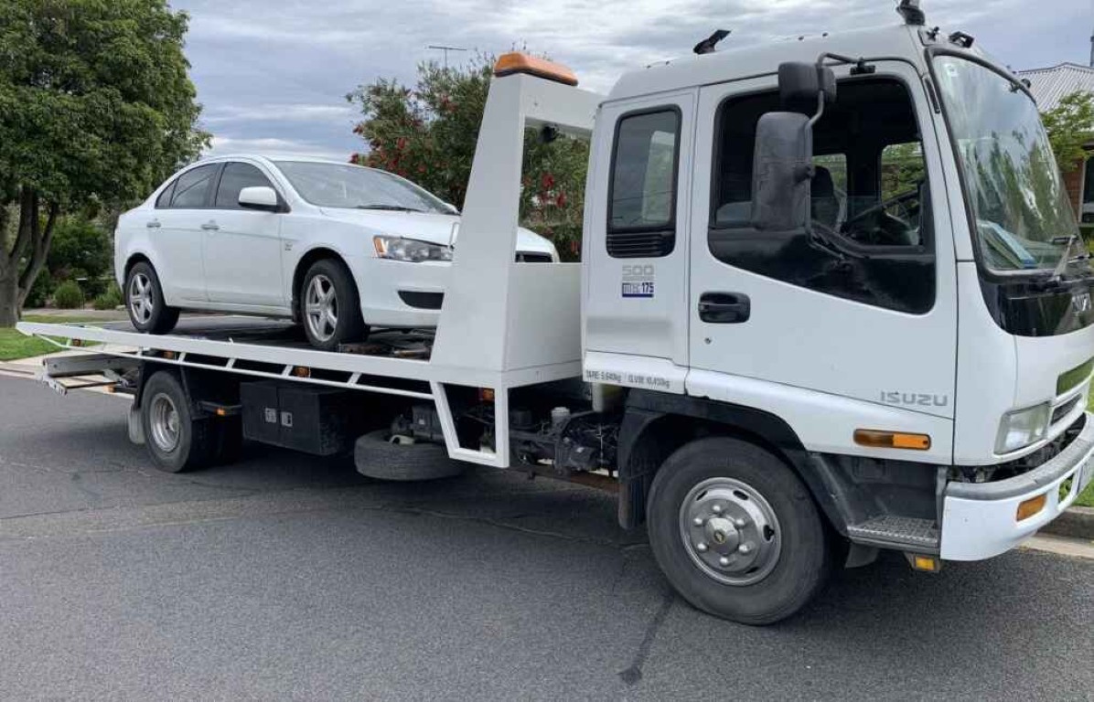 Tow truck operator assisting with battery replacement for a white sedan